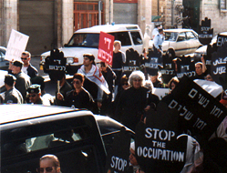 Gila with her white hair is visible among the demonstrators in front